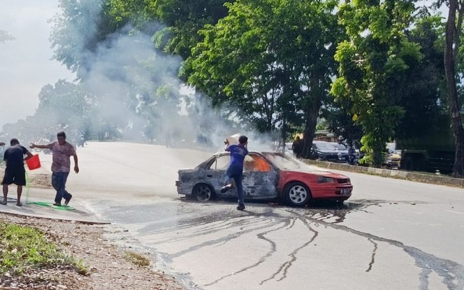 
					Warga berusaha menyiramkan air ke mobil yang terbakar di SPBU Doco Sagulung